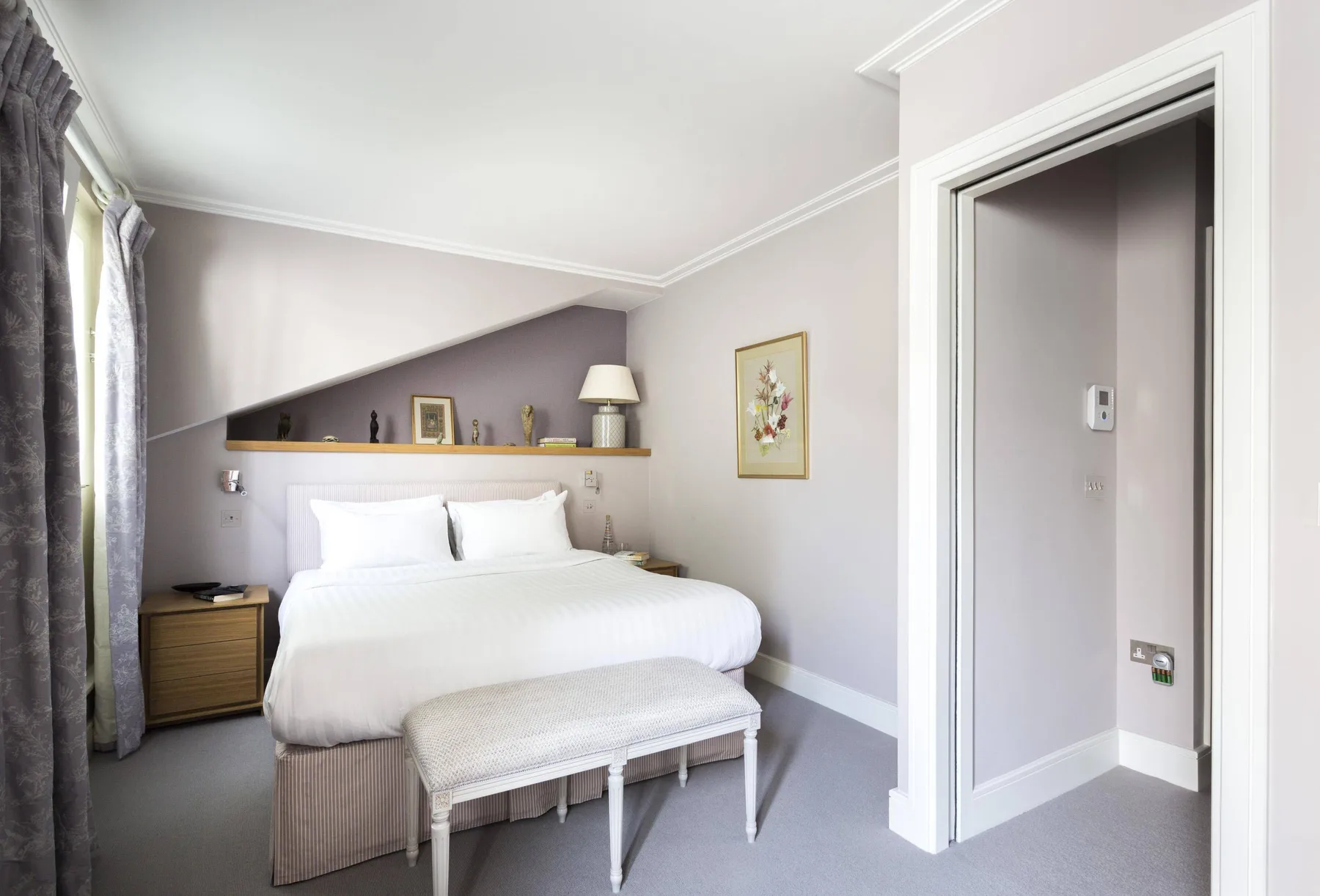 A bedroom with a neatly made bed and a small upholstered bench at its foot.