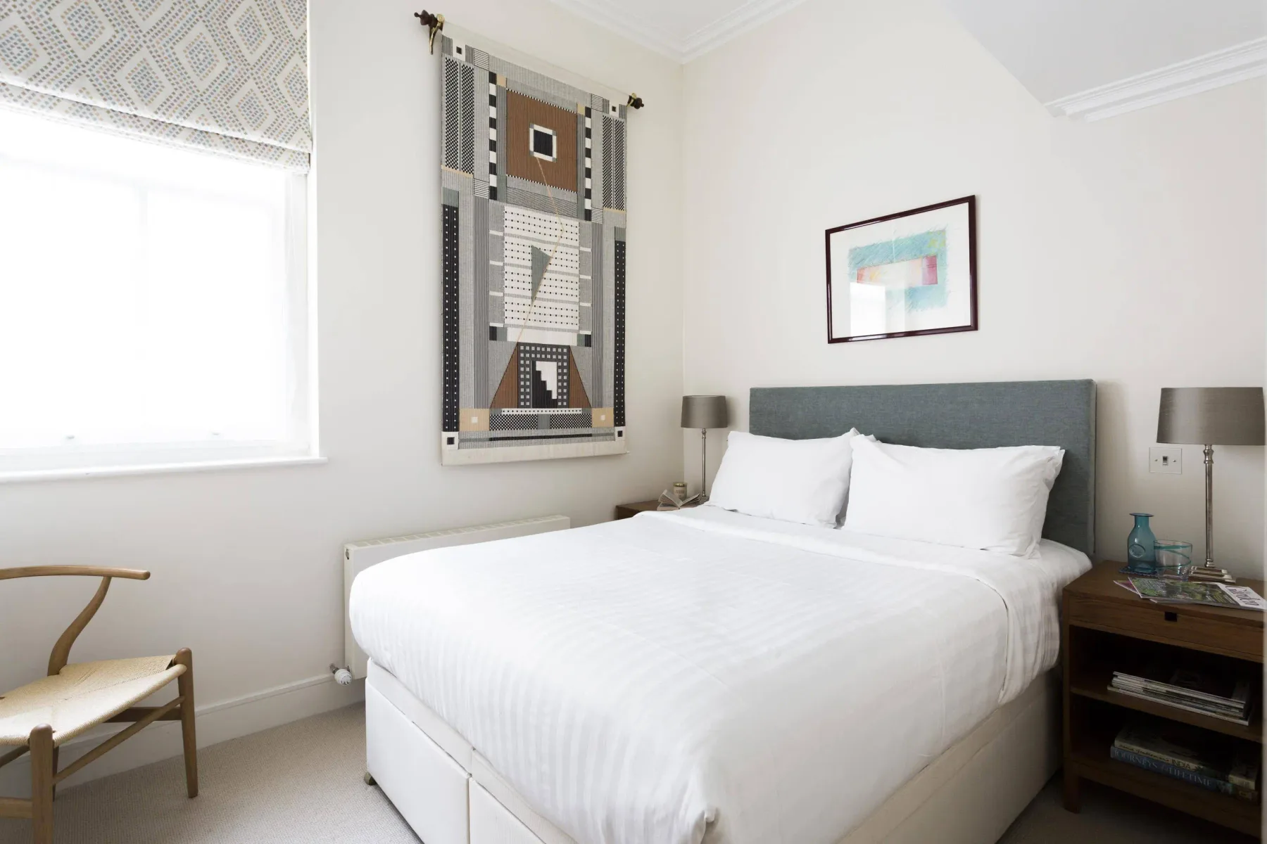 A bright bedroom with a neatly made bed and patterned wall hanging.