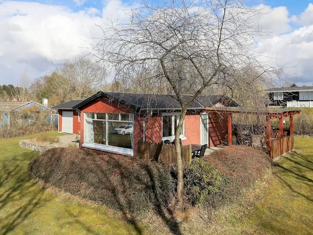 Una casa roja de una planta se encuentra en un patio con césped bajo un árbol sin hojas.