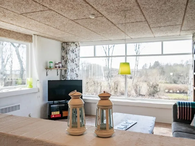 Una sala luminosa con grandes ventanas que dan a unos árboles y un televisor.