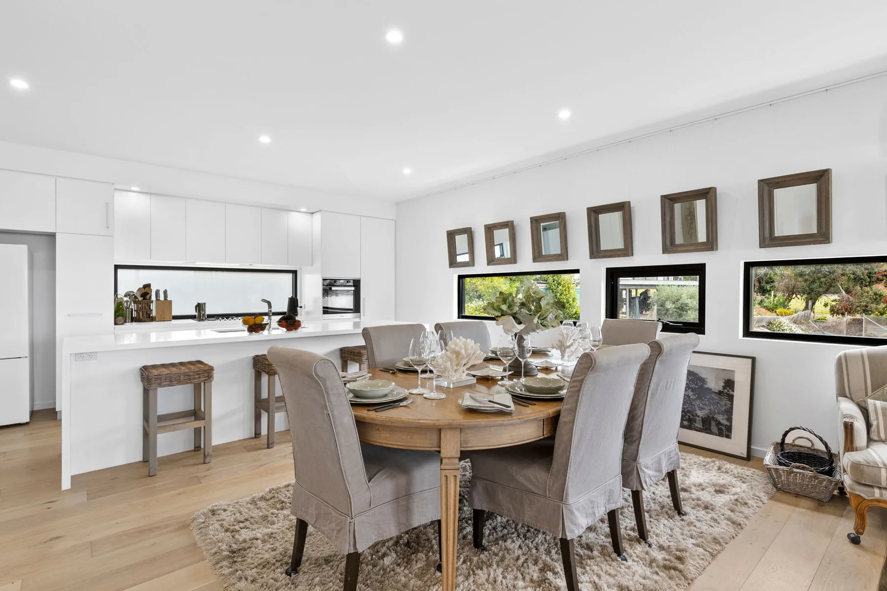 Comedor con la mesa puesta junto a una cocina blanca y luminosa.