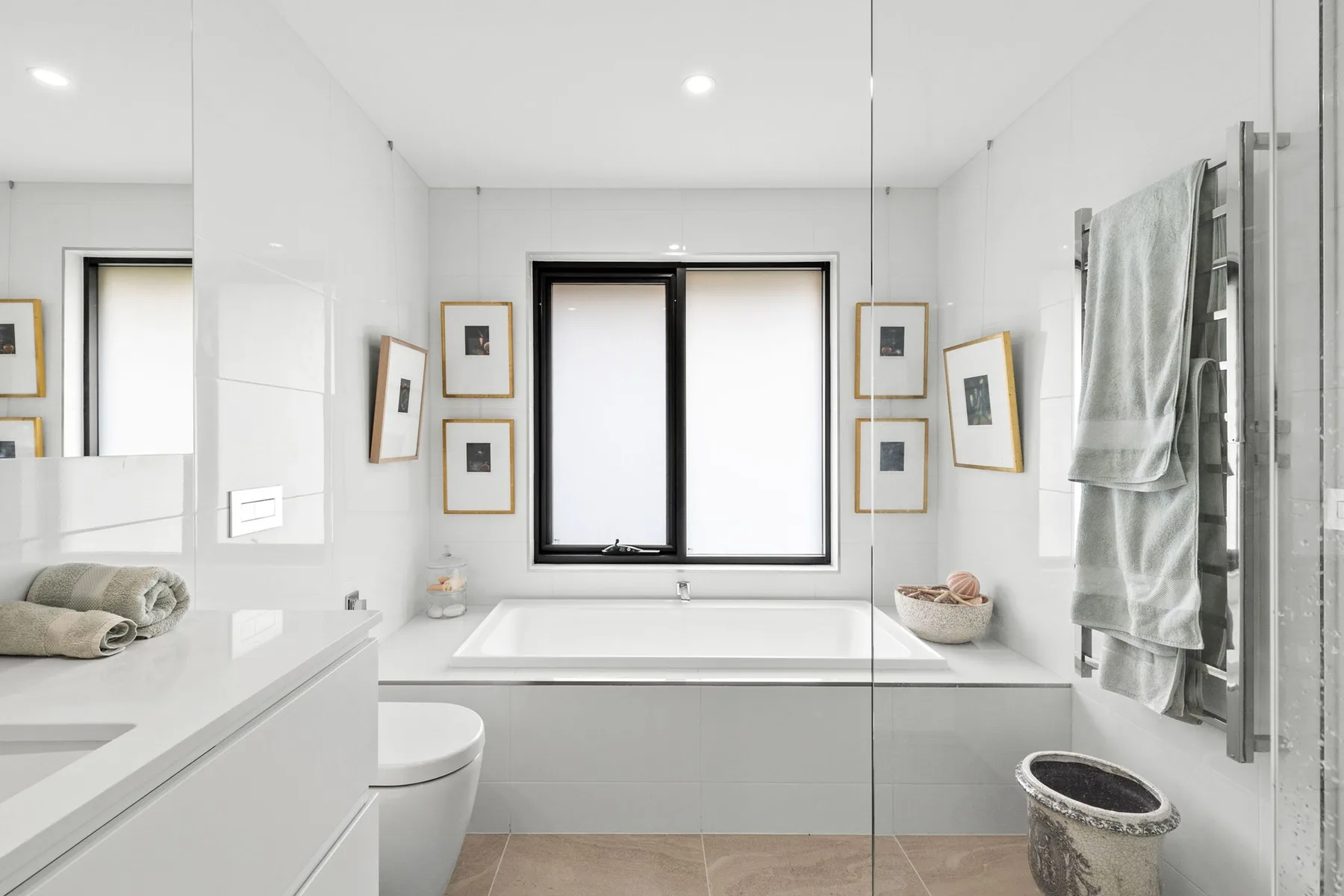 Un baño luminoso con una bañera bajo una ventana y una ducha de cristal.