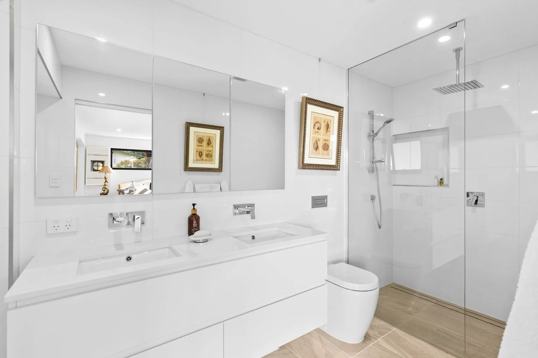 Un baño luminoso con un mueble de lavabo largo y una ducha acristalada.