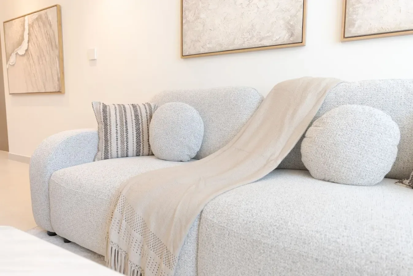 Una sala luminosa con un sofá claro y una manta extendida.