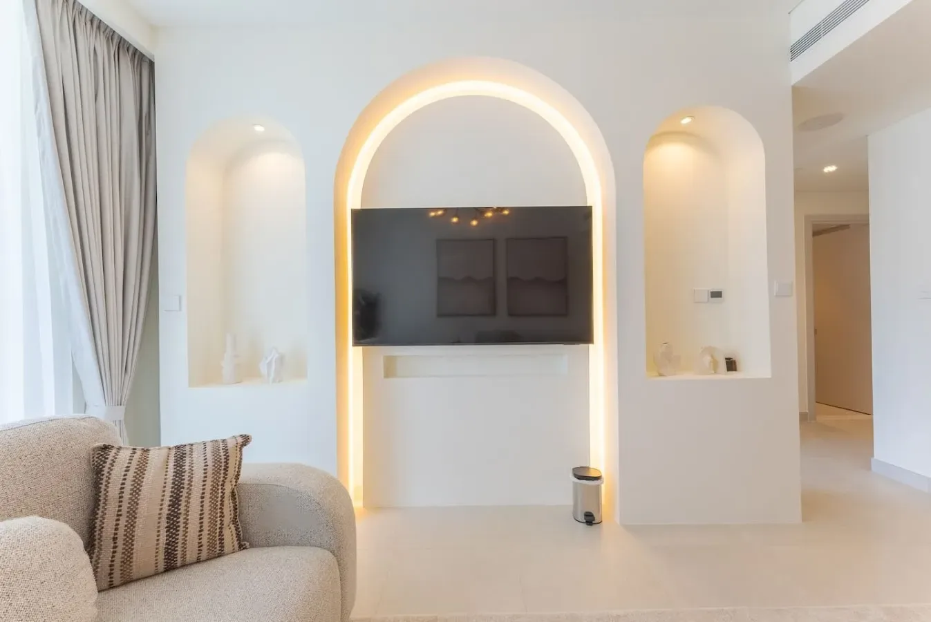 Una sala luminosa con un televisor en un nicho arqueado e iluminado.