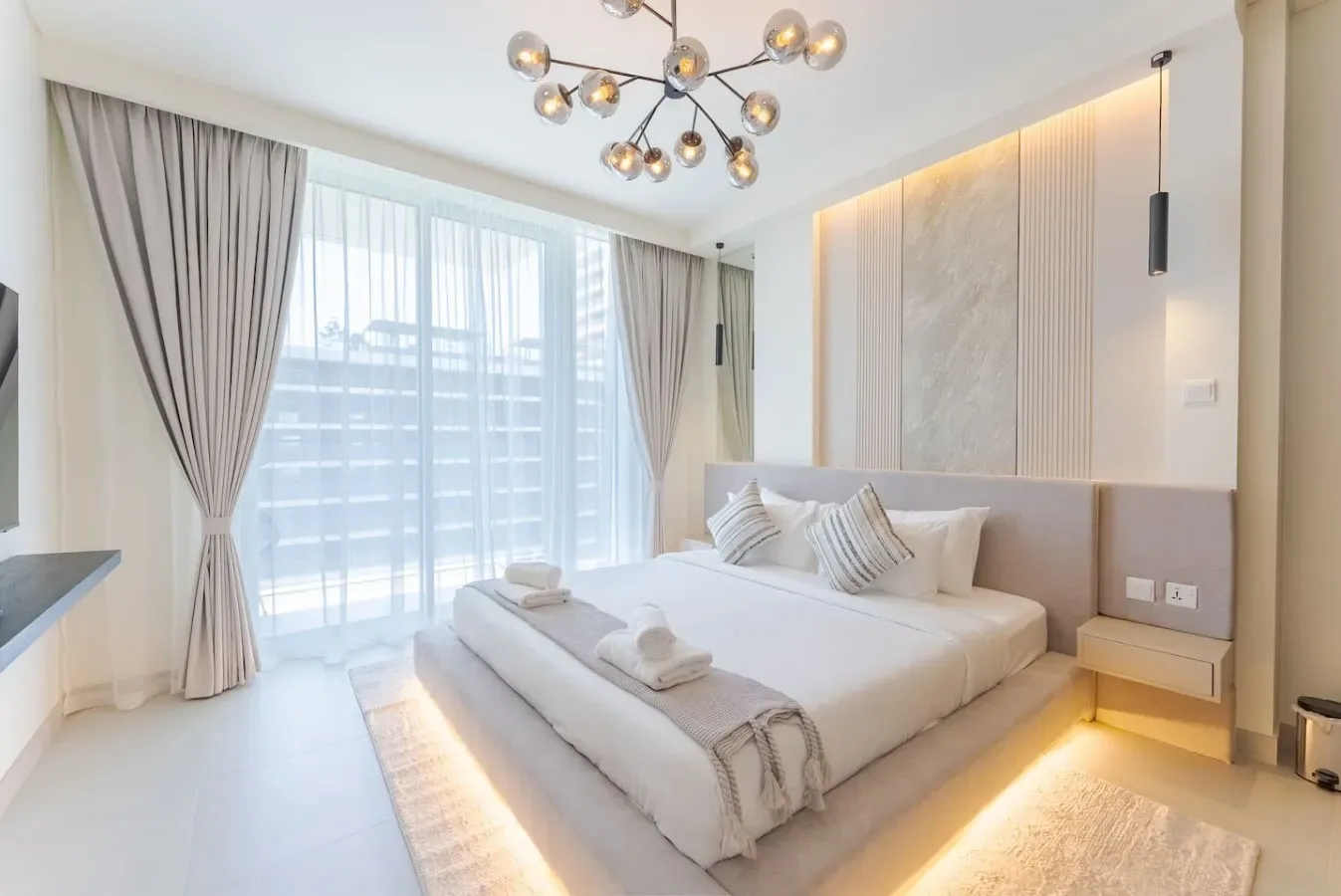 Un dormitorio luminoso con una cama bien hecha junto a ventanas de suelo a techo.