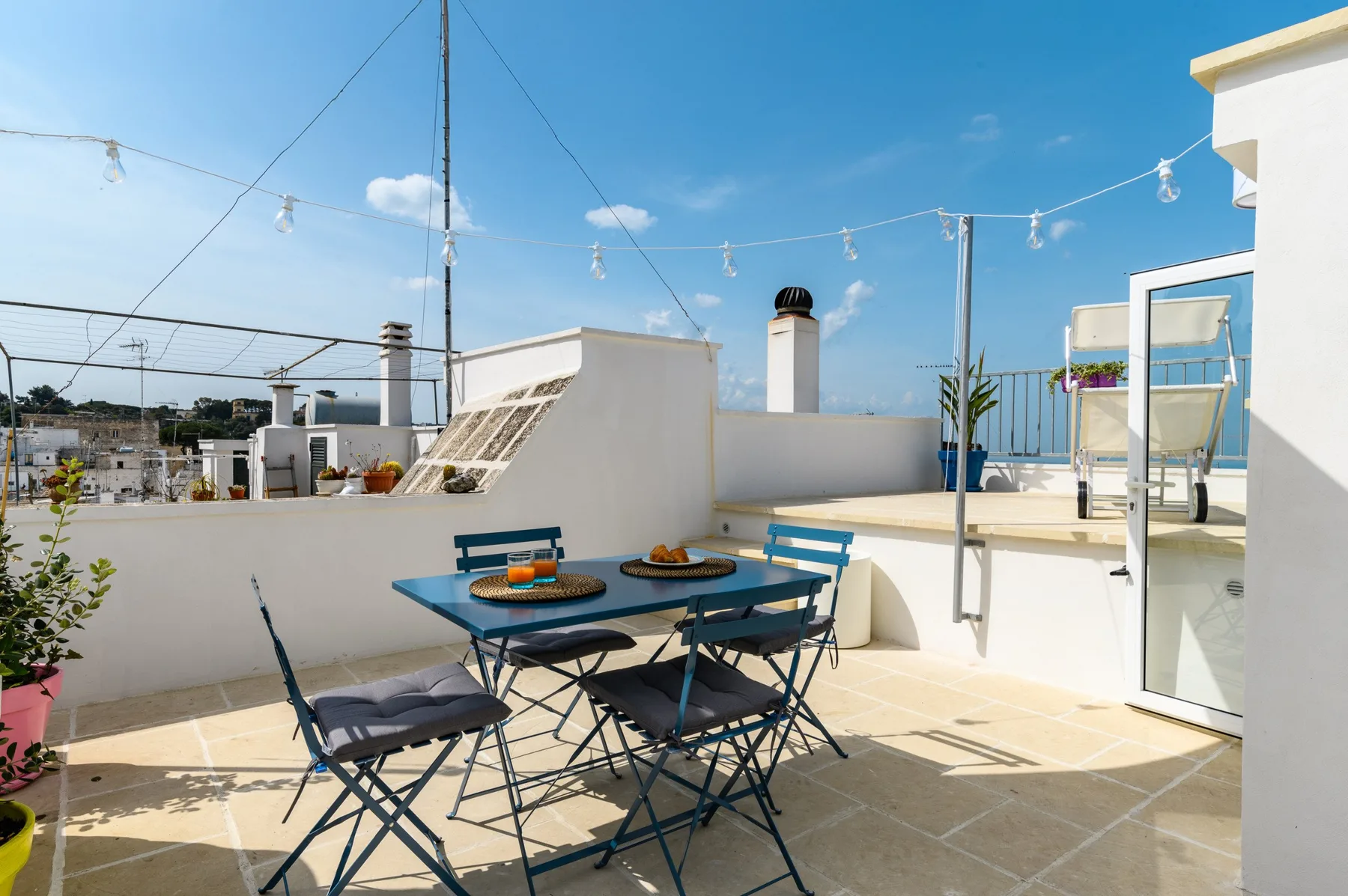 A rooftop terrace with a dining table and chairs beneath string lights.