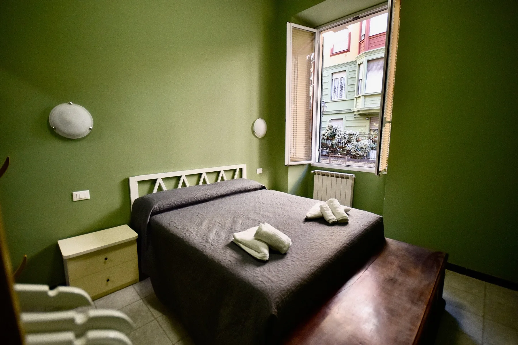 A bedroom with a bed and an open window overlooking the street.