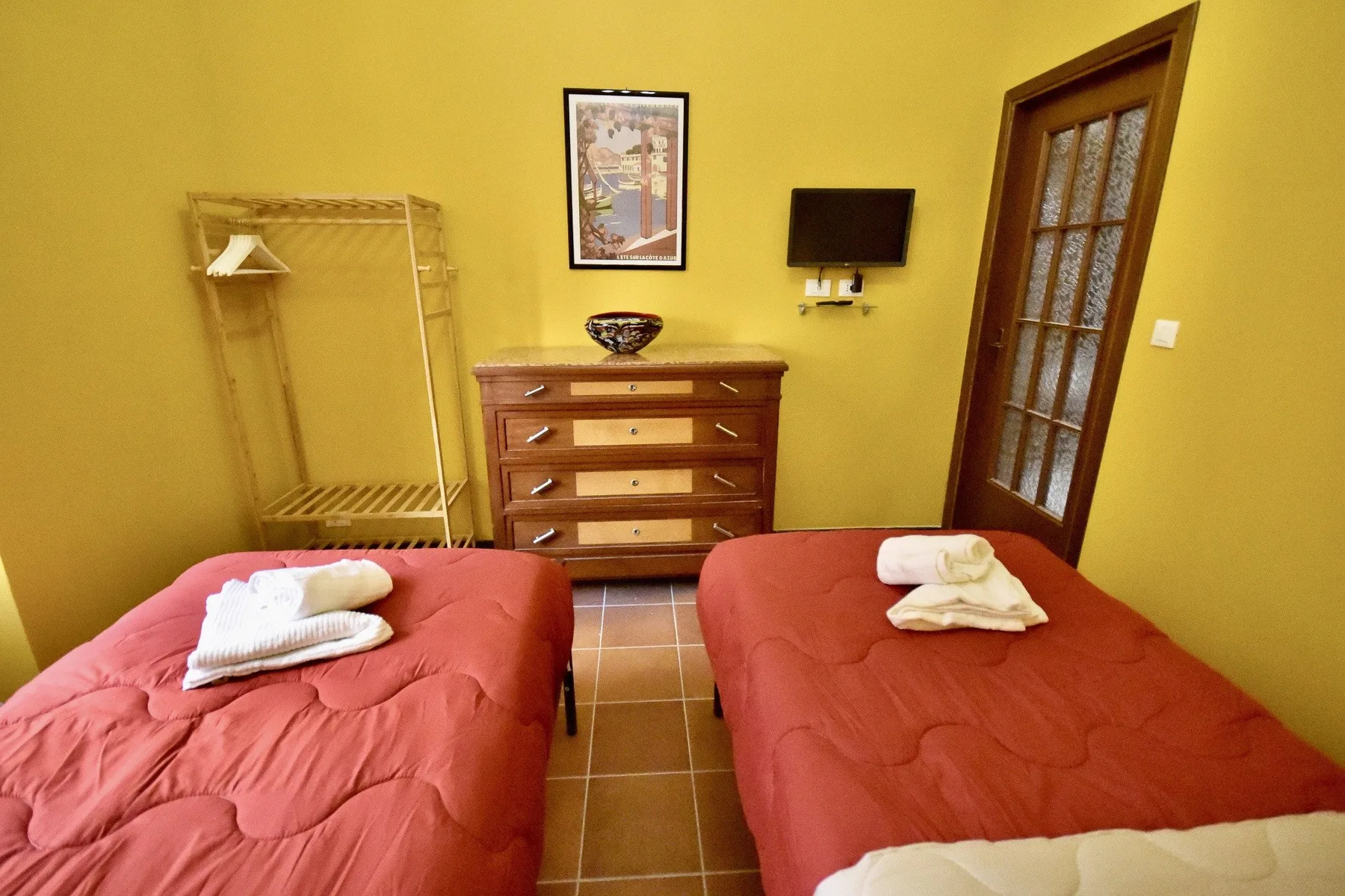 A bedroom with two beds, a wooden dresser, and a wall-mounted television.