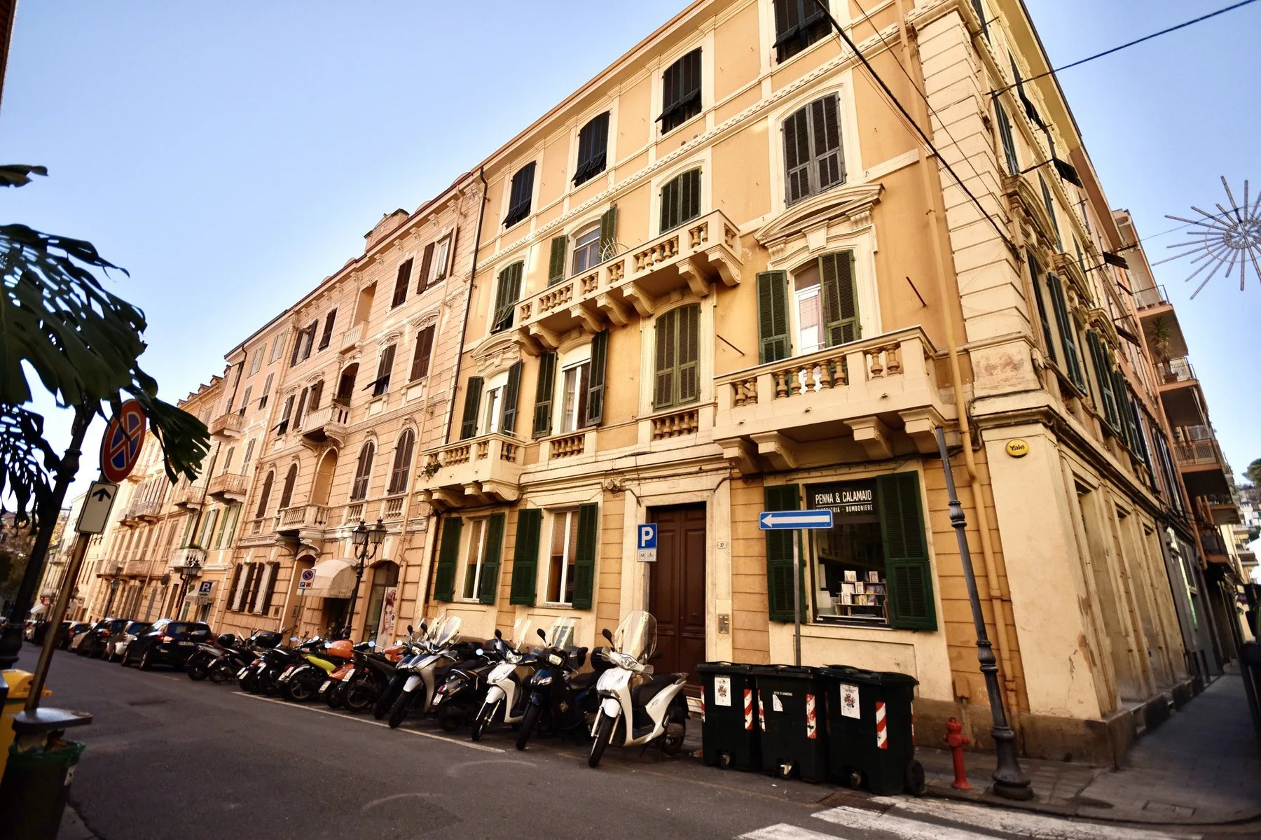 A street scene with a multi-story building and parked scooters along the sidewalk.