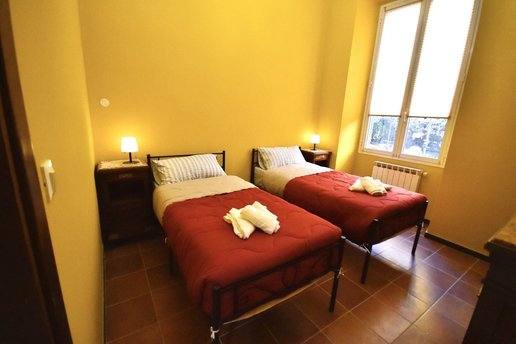 A bedroom with two beds, red bedspreads, and a large window.