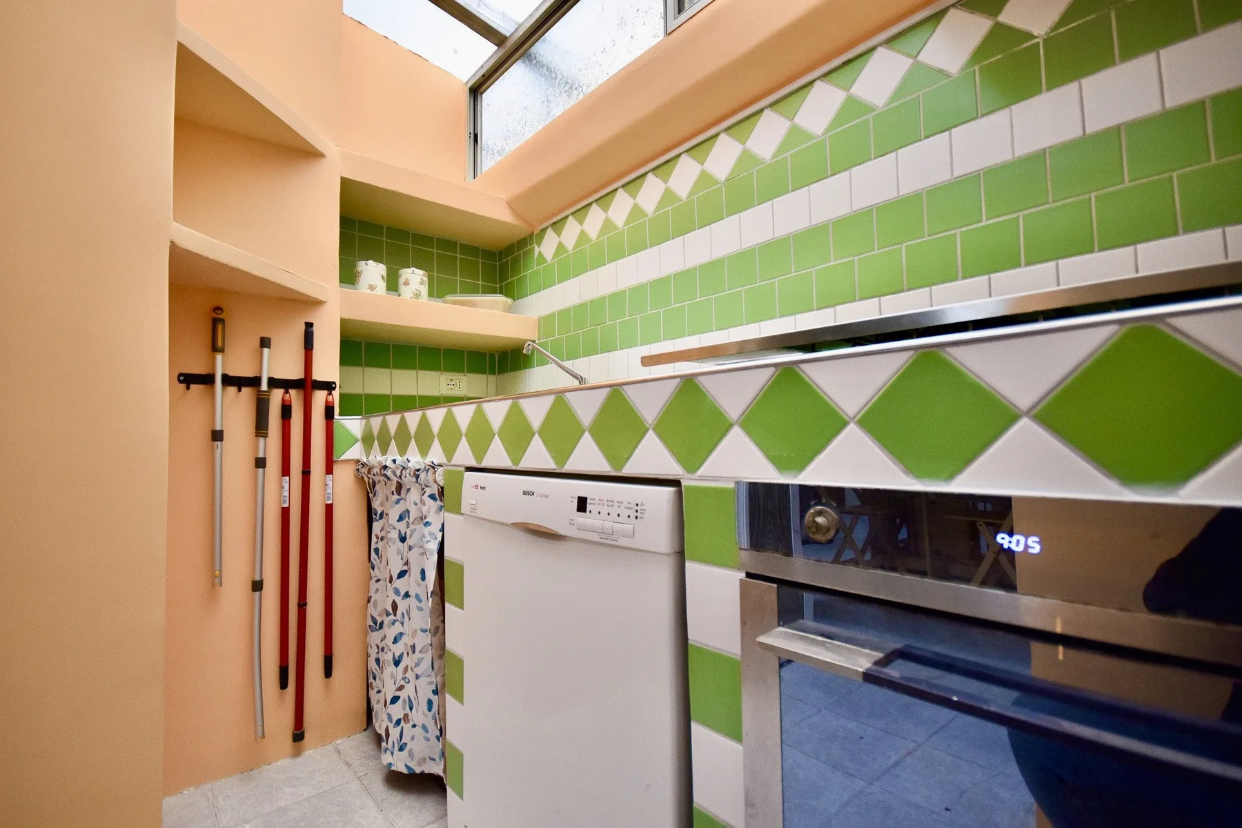 A laundry area with a washing machine beneath green tiled walls and a skylight.