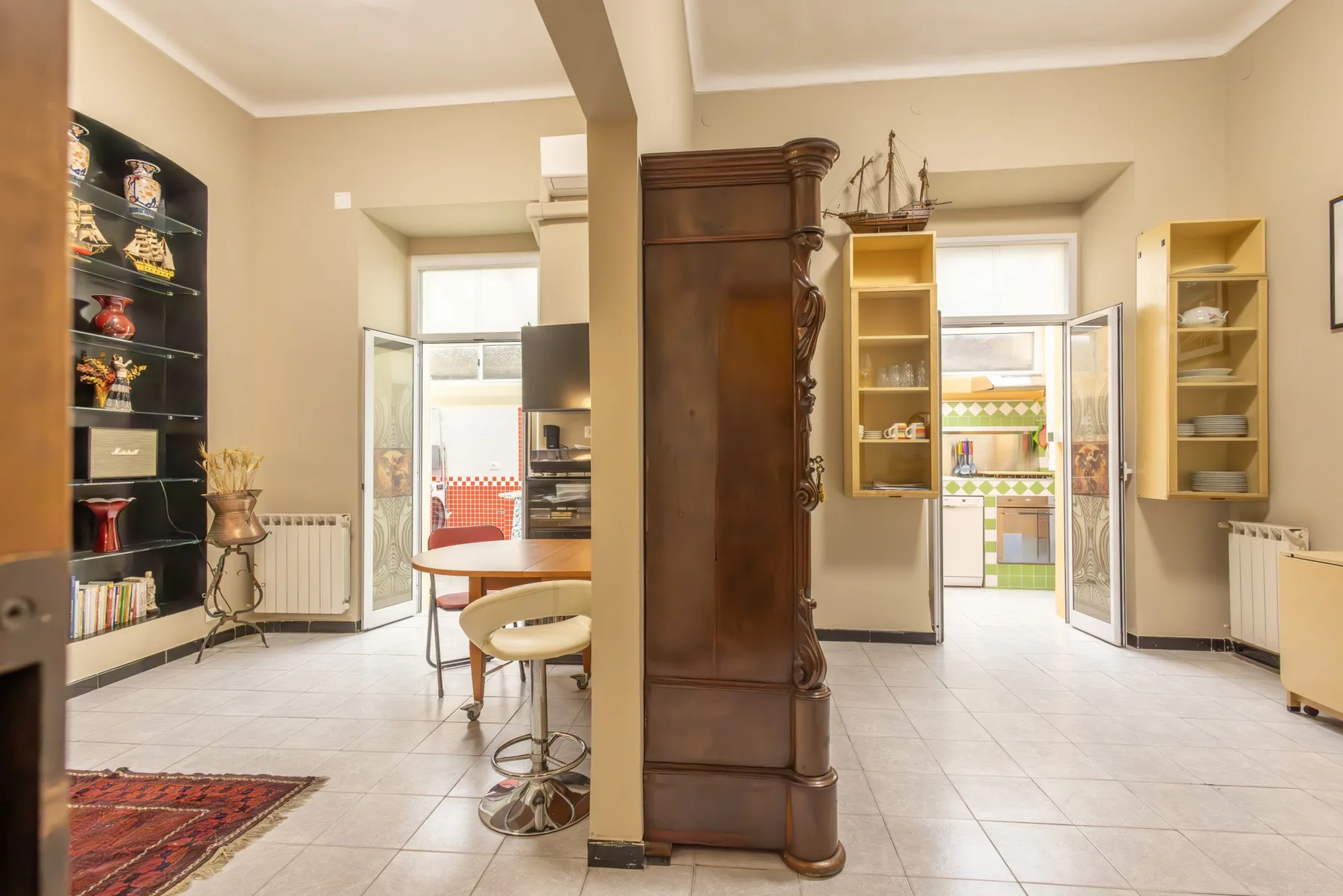 A bright interior room with display shelves, a central wooden cabinet, and tiled flooring.