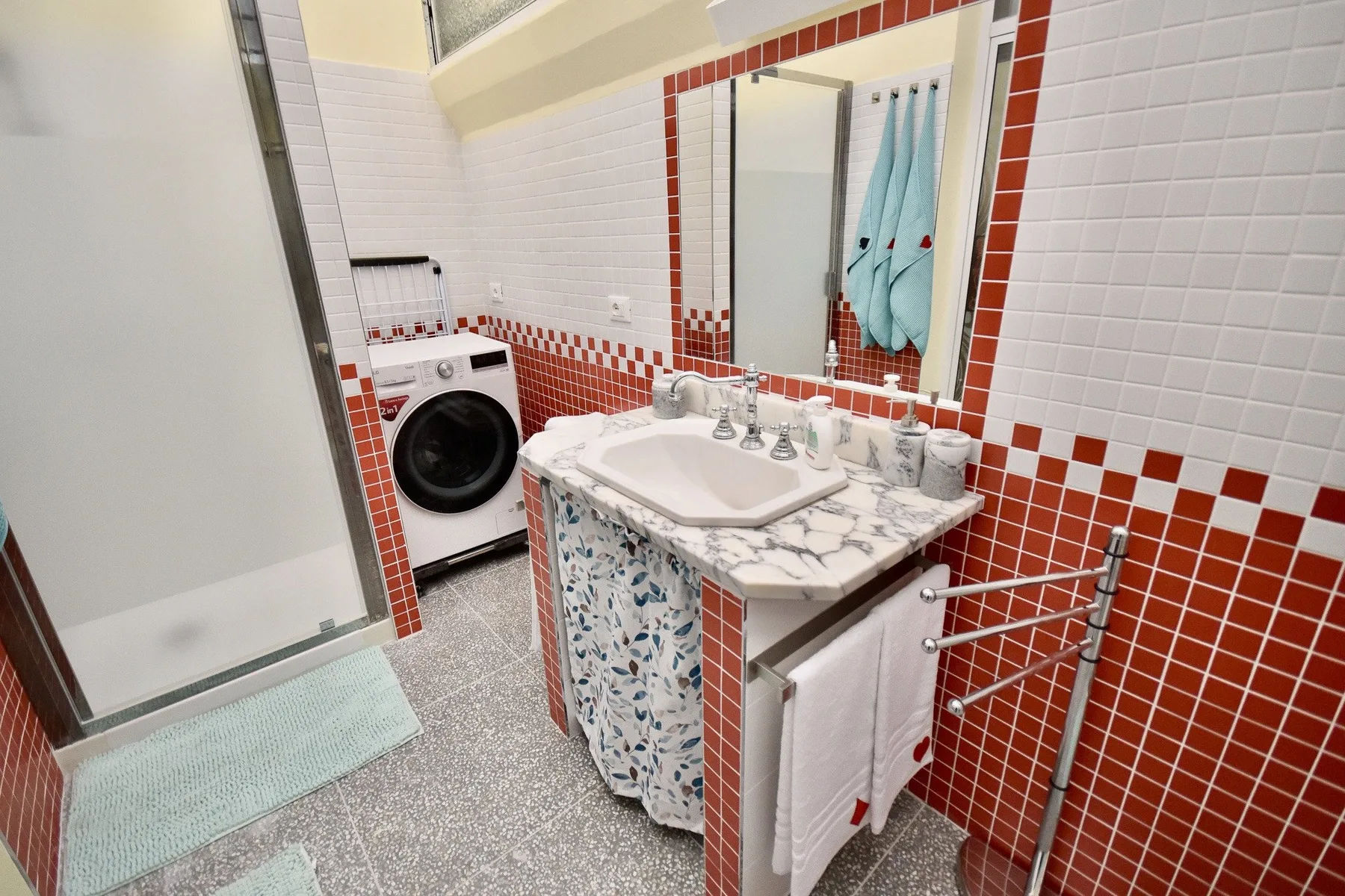 A tiled bathroom with a sink, mirror, and washing machine.