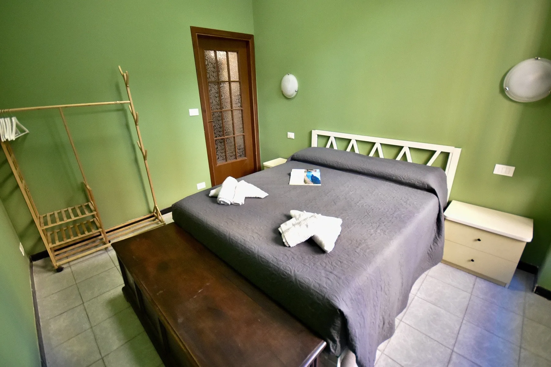 A green-walled bedroom with a bed and a wooden clothes rack.