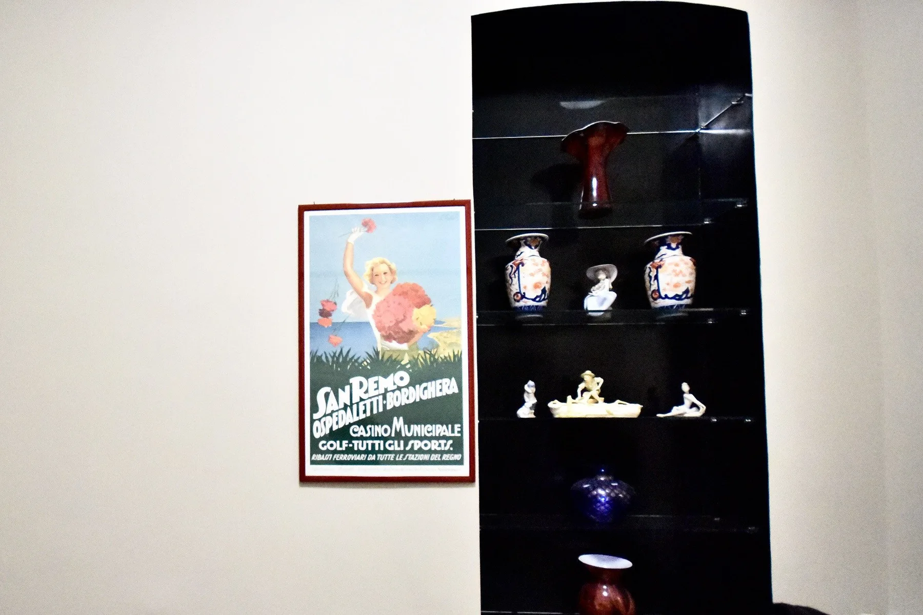 A framed poster hangs beside a dark display cabinet of decorative objects.