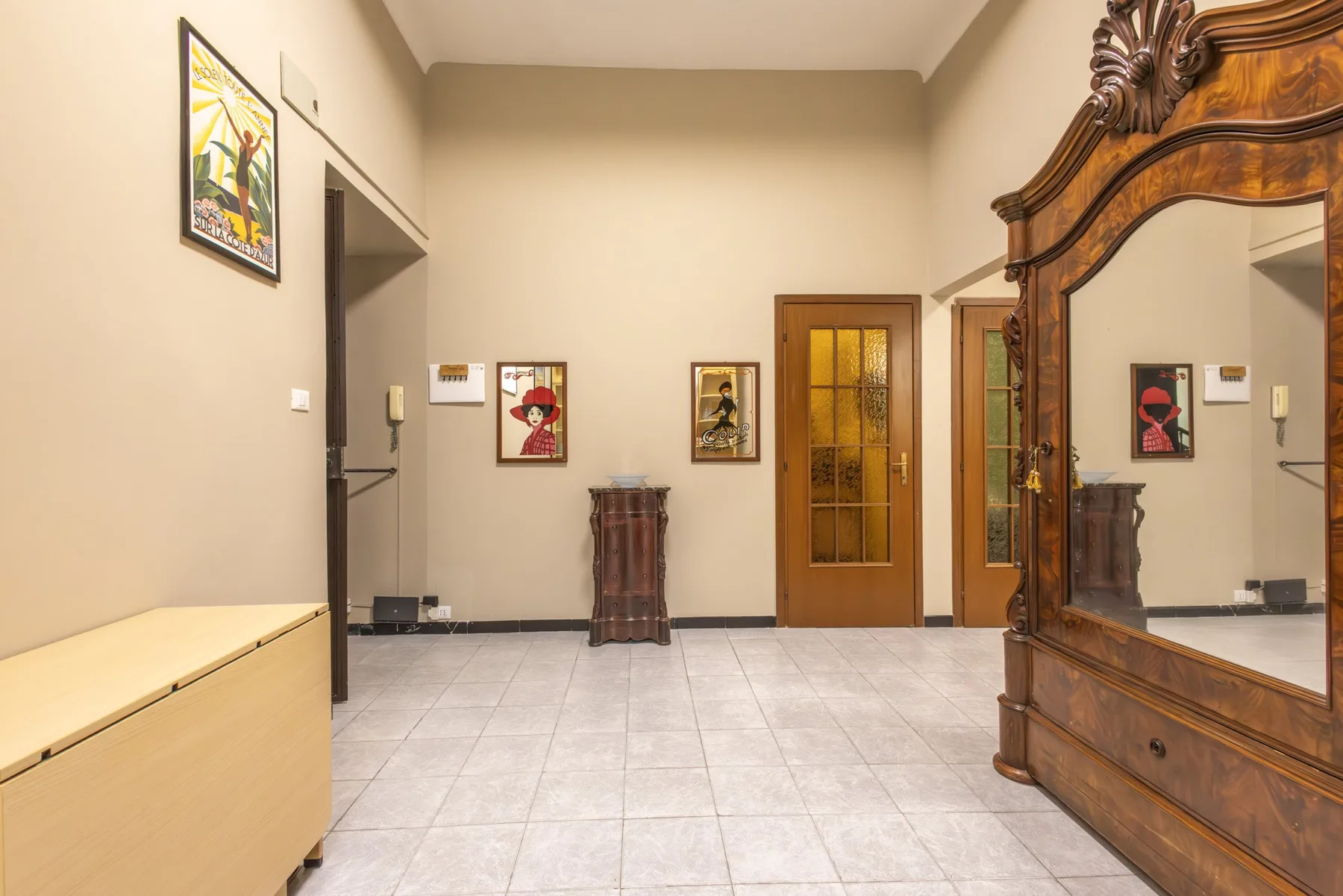 A tiled interior hallway with framed artwork and a wooden door.