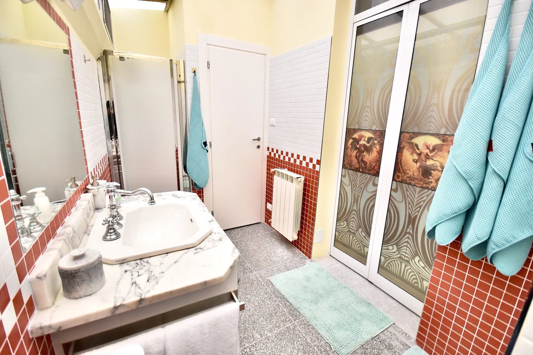 A bathroom with a marble-look sink counter, tiled walls, and a glass shower enclosure.