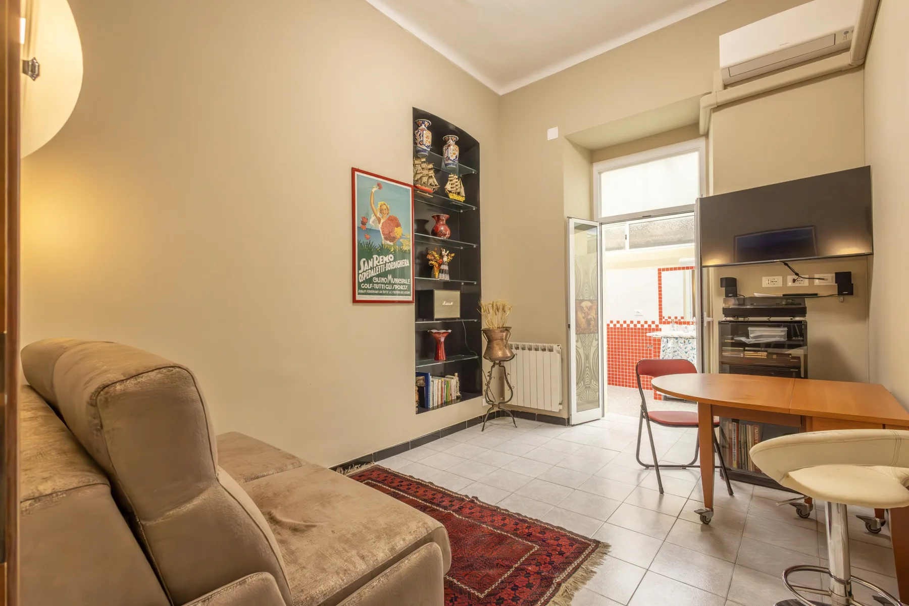 A living area with seating, a dining table, and a kitchen visible in the background.