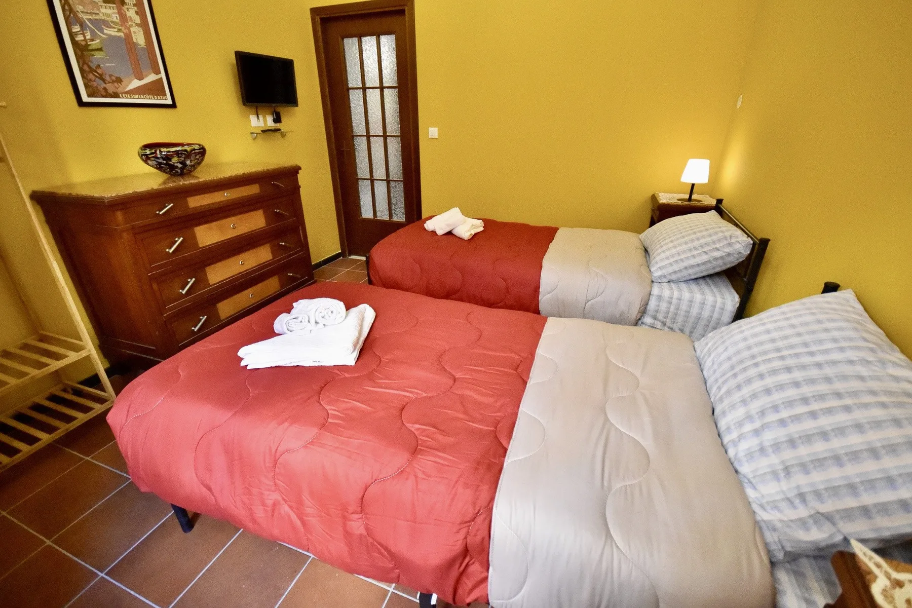 A bedroom with two beds dressed in red and gray bedding.