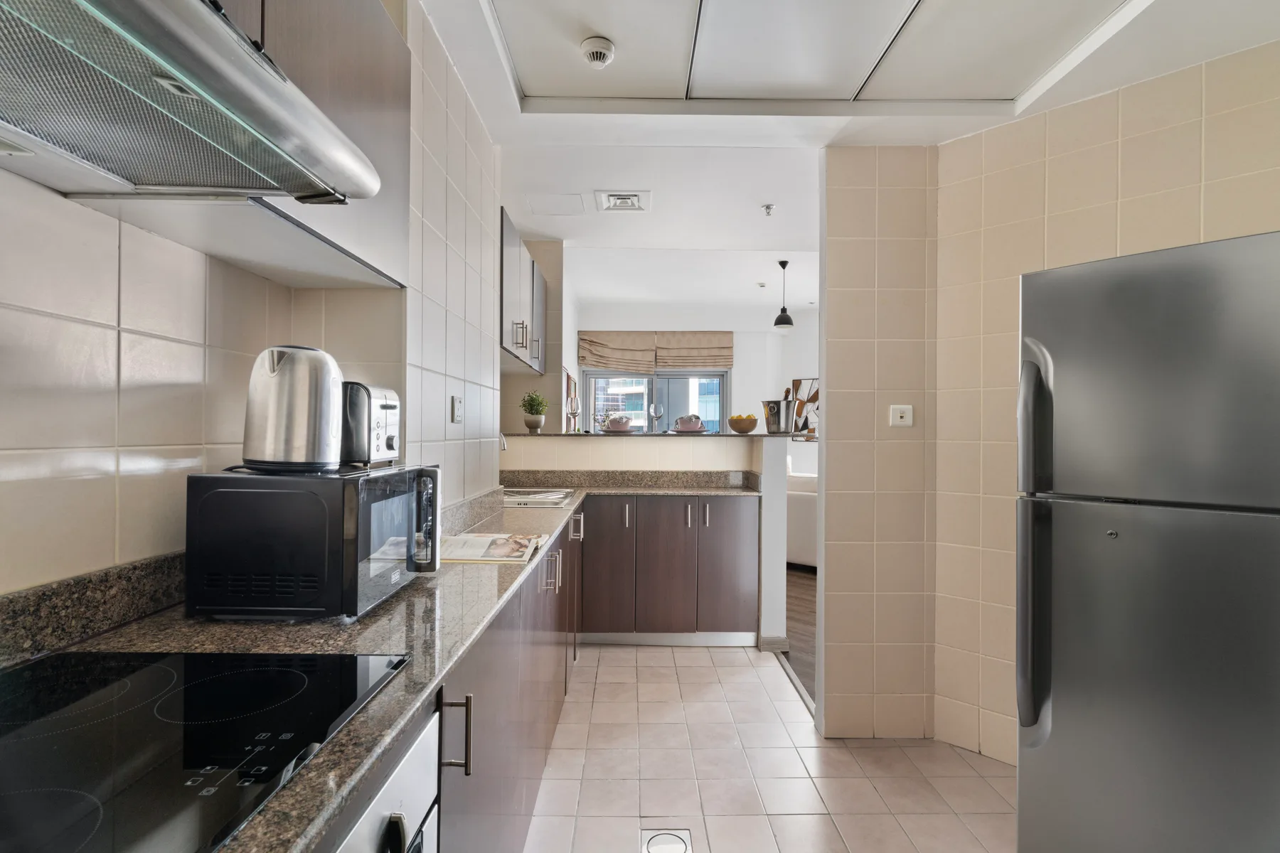 Una cocina con azulejos, encimeras oscuras, electrodomésticos y un refrigerador.