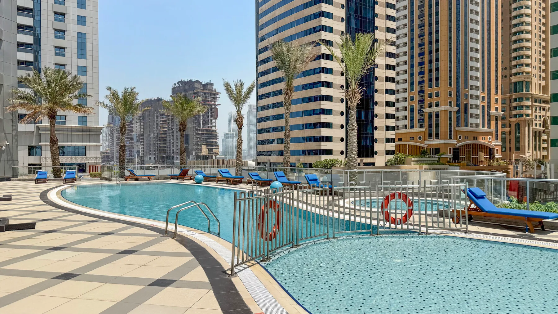 Una piscina junto a edificios altos, con palmeras a lo largo de la terraza.