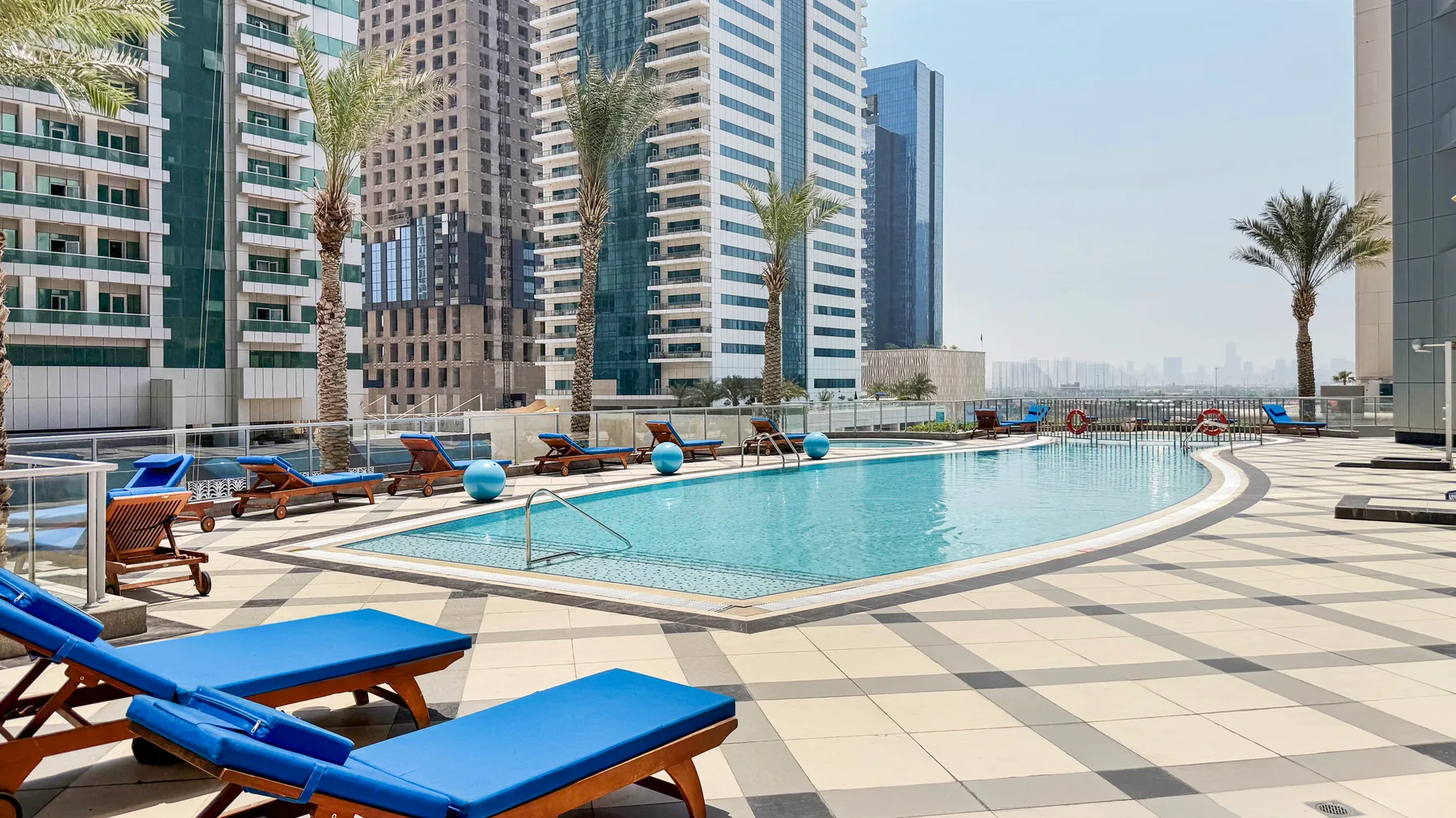 Una piscina al aire libre con tumbonas azules sobre una terraza pavimentada.
