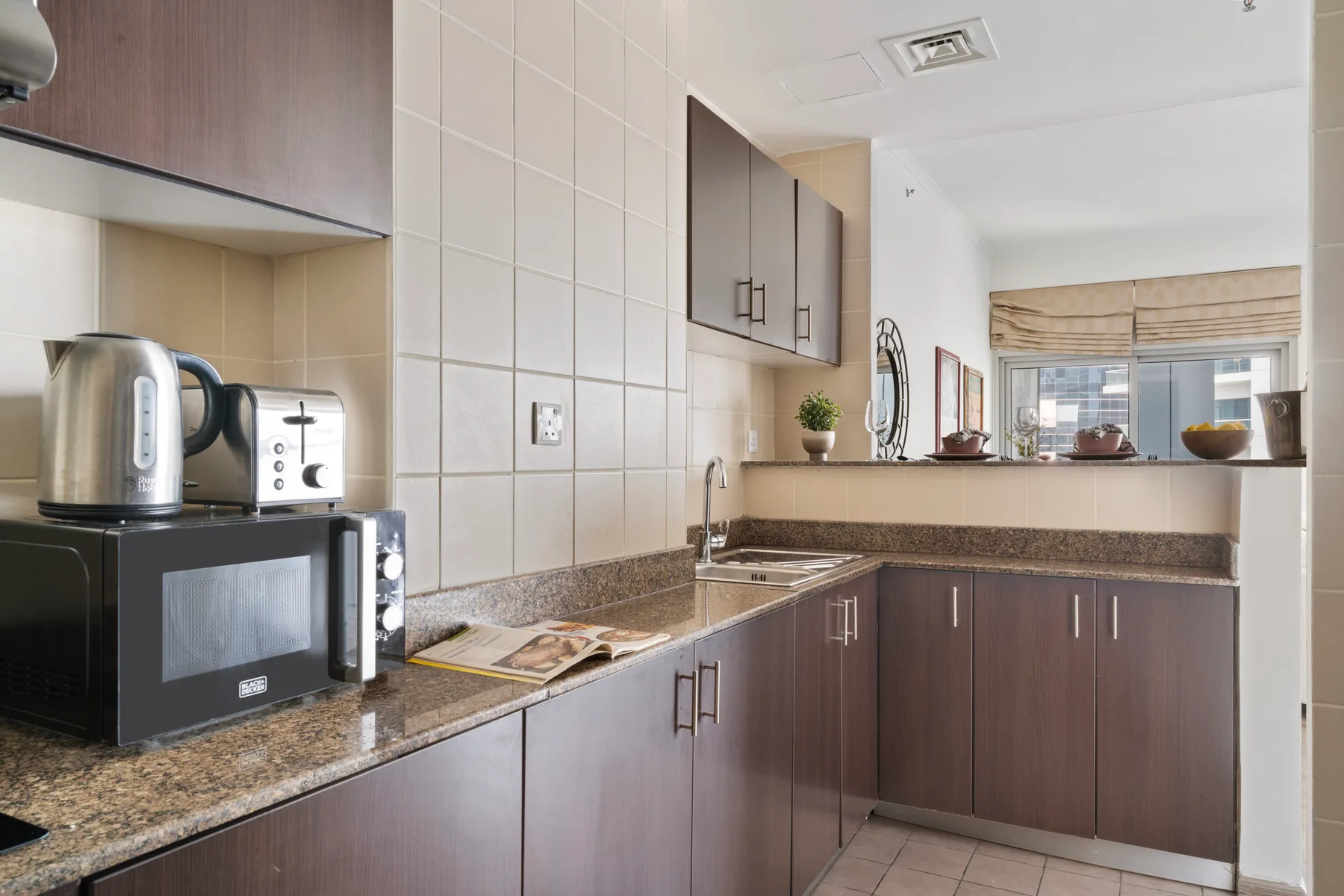 Una cocina compacta con gabinetes oscuros, salpicadero de azulejos y electrodomésticos sobre la encimera.