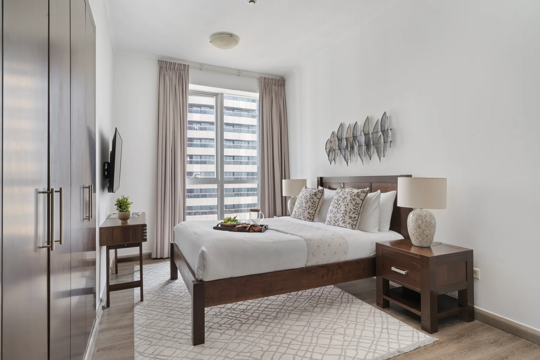 Un dormitorio luminoso con una cama tendida y una gran ventana con cortinas.