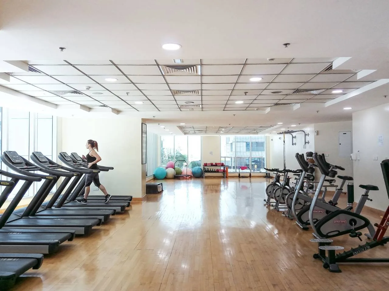 Un gimnasio con cintas de correr y bicicletas estáticas a los lados de una sala luminosa.