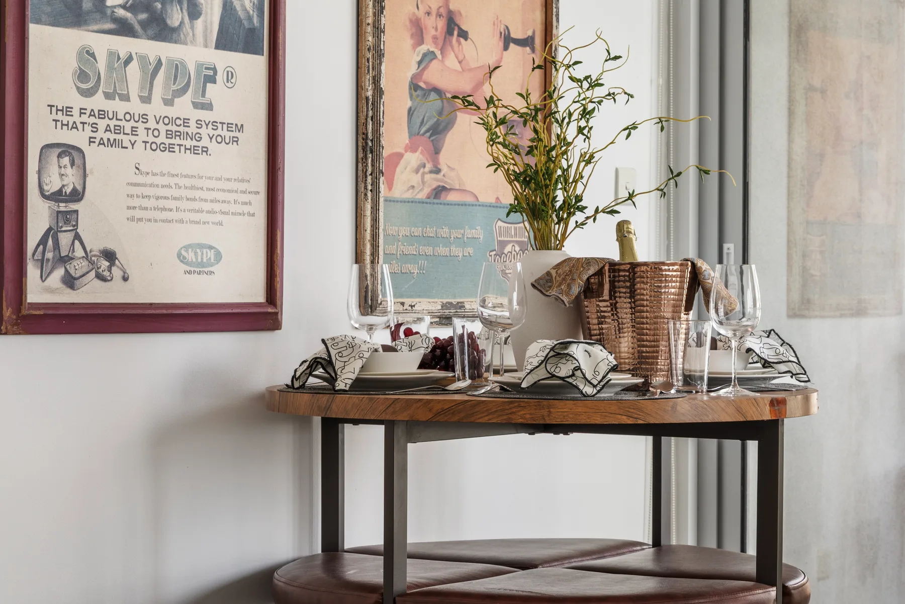 Una pequeña mesa de comedor está preparada con copas y servilletas dobladas bajo cuadros enmarcados.