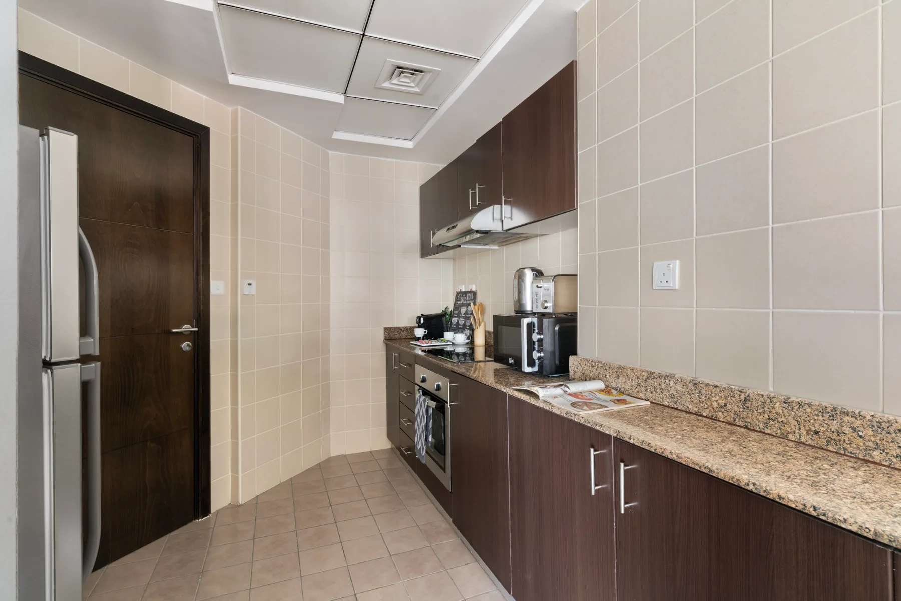 Una cocina con azulejos, gabinetes oscuros, una encimera y pequeños electrodomésticos.