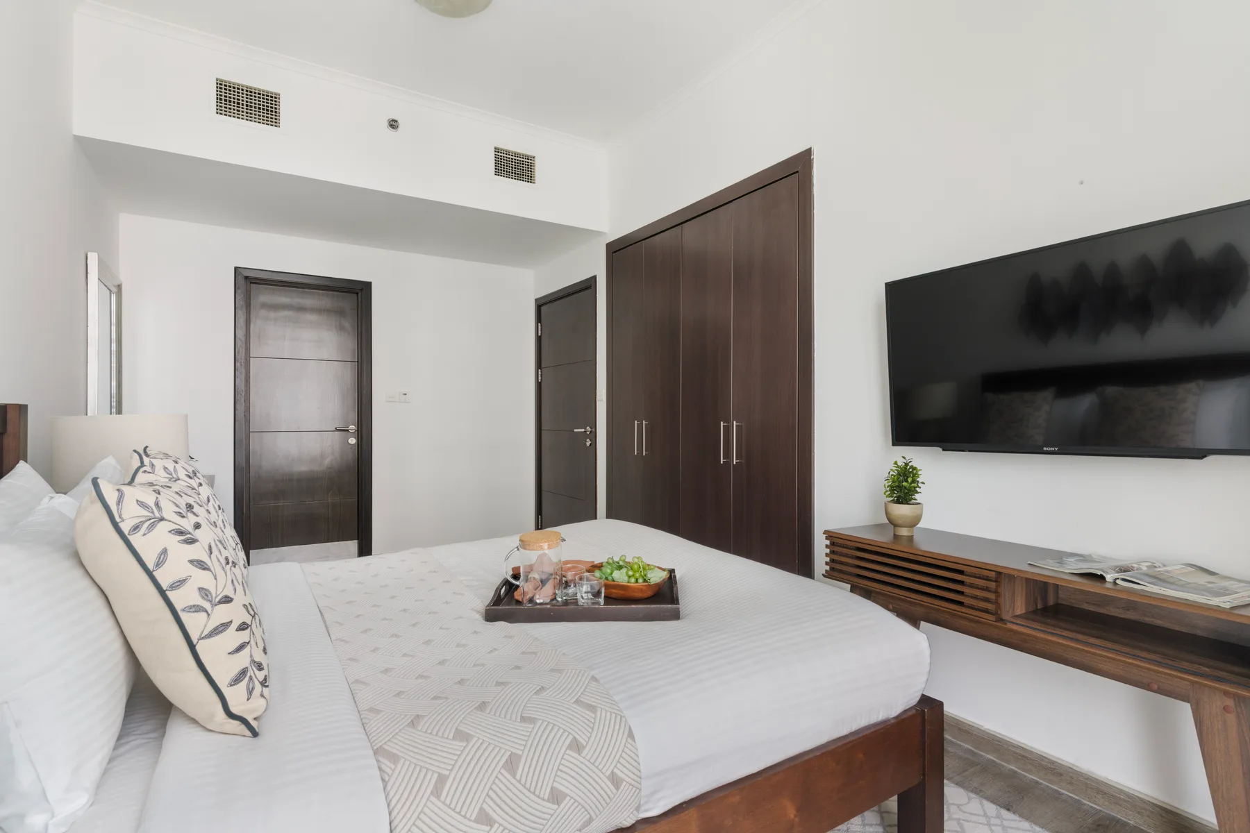 Un dormitorio con una cama bien arreglada, armarios oscuros y un televisor en la pared.