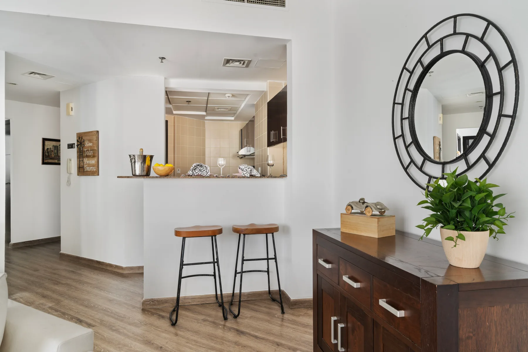 Un interior luminoso muestra una barra hacia la cocina con dos taburetes y una consola de madera.