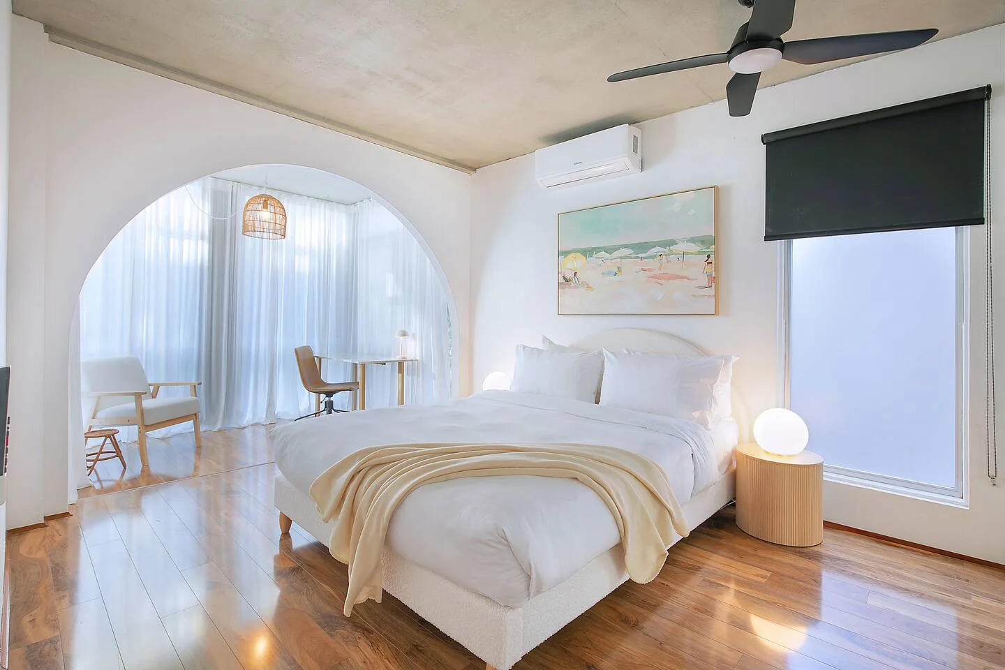 Un dormitorio luminoso con una cama, un ventilador de techo y un arco que da a una zona de estar.