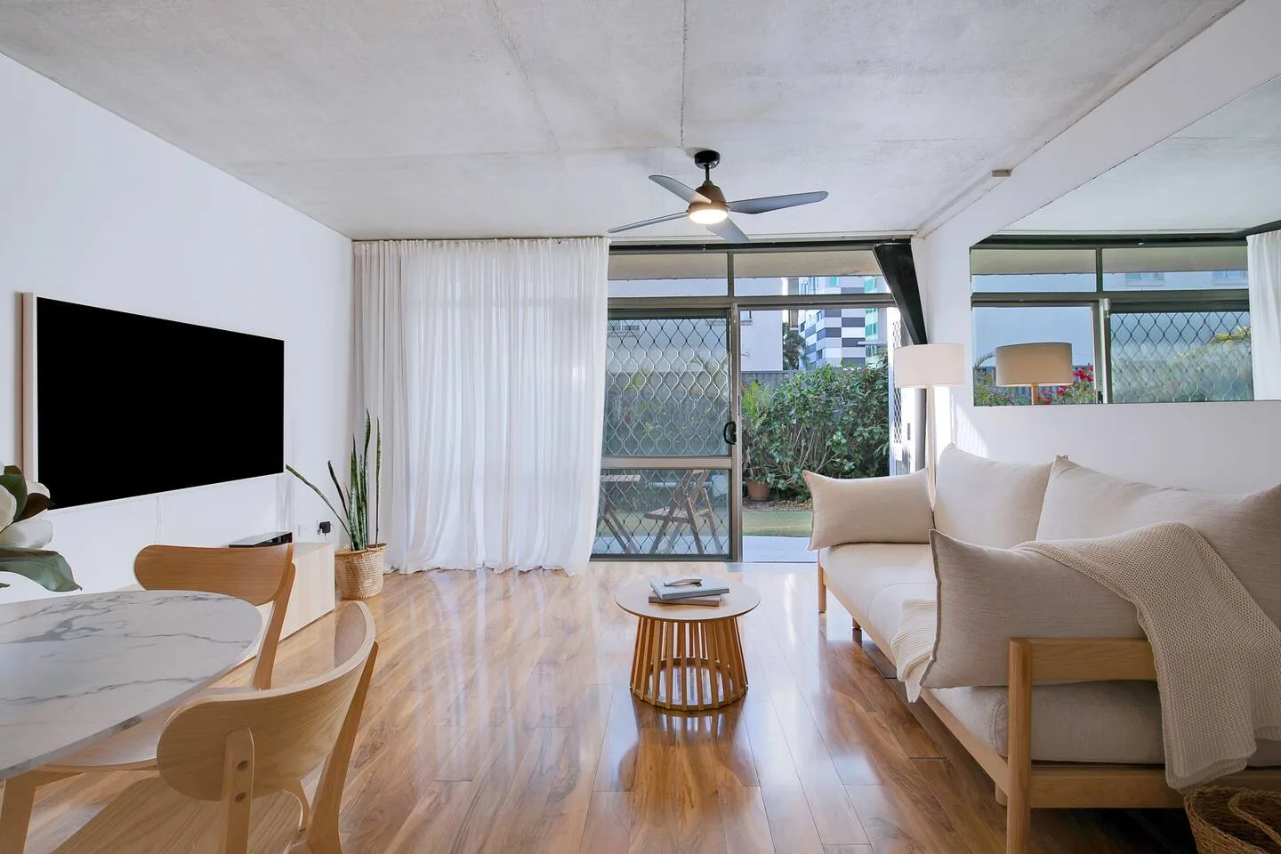 A bright living room has seating, a dining table, and sliding glass doors opening to greenery.