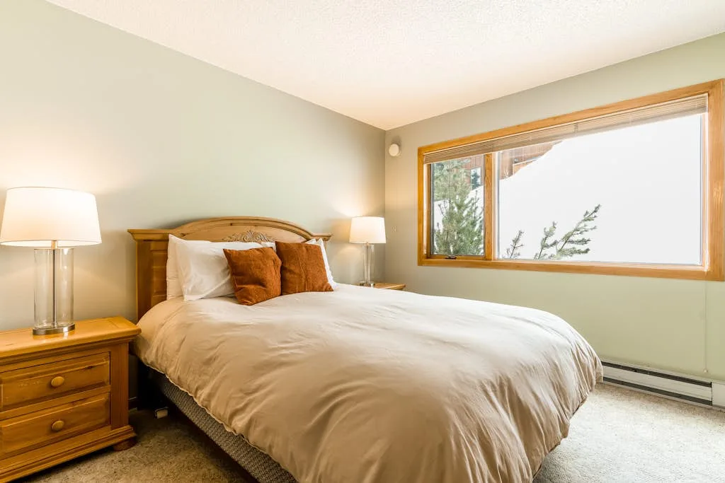 A bedroom with a bed, bedside tables, and a large window.