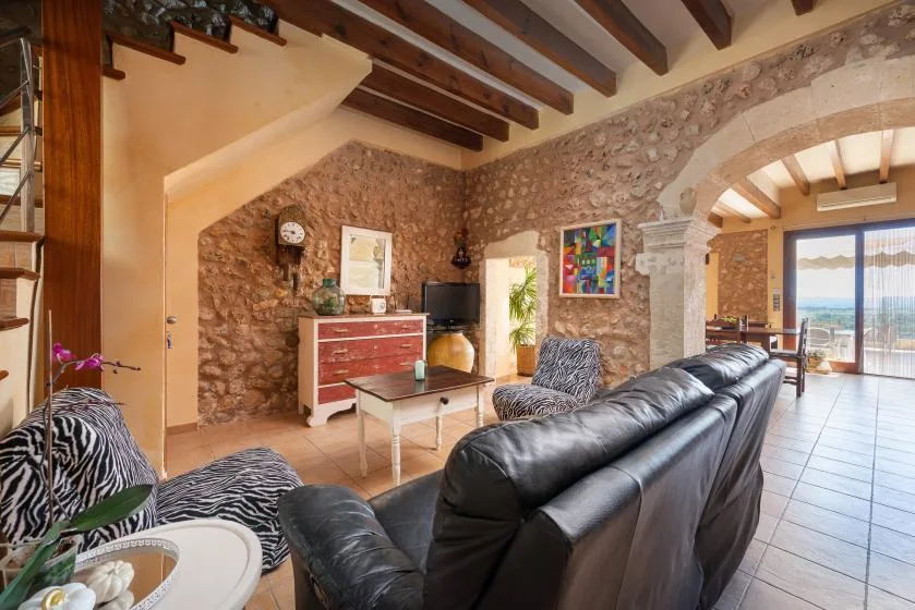 A living room with dark seating, stone walls, and exposed ceiling beams.