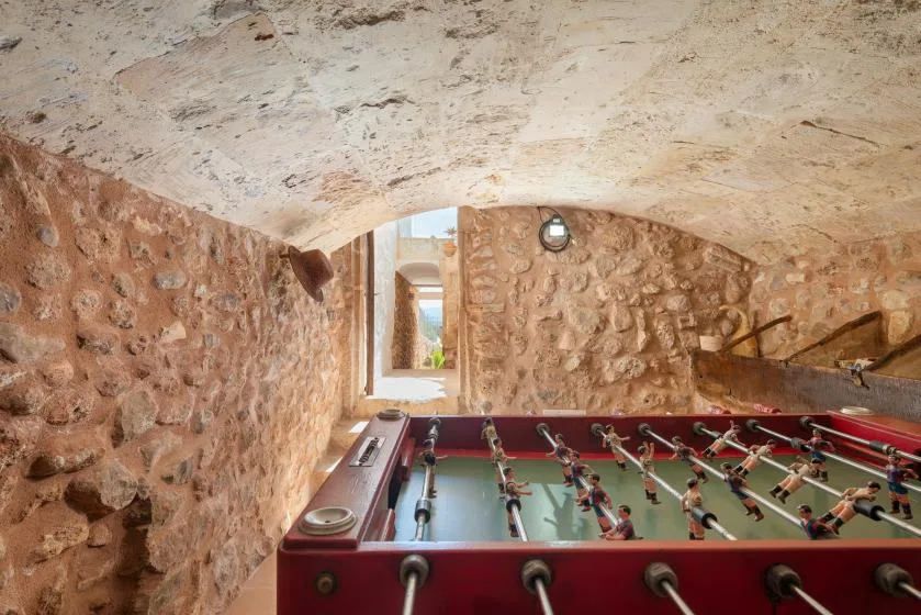 A foosball table sits in a rustic stone room beneath a low arched ceiling.