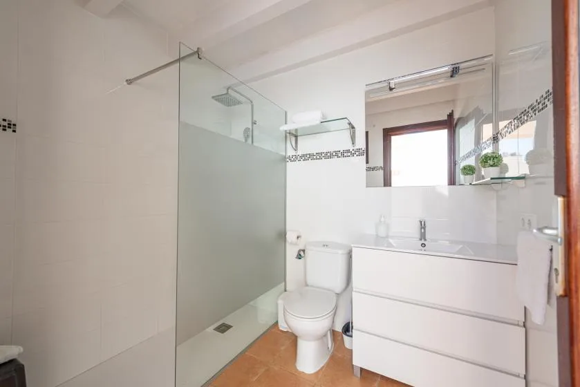 A bright bathroom with a glass shower, toilet, and vanity.