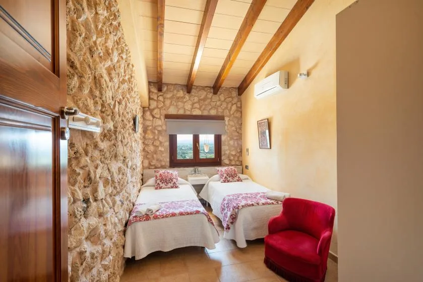 A bedroom with two beds, exposed ceiling beams, and a red upholstered chair.