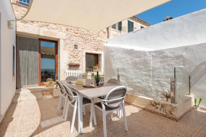 A sunny outdoor dining area with a table and chairs beneath a shade canopy.