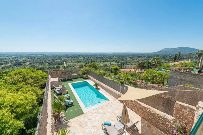 An outdoor pool sits in a walled terrace overlooking a green landscape.