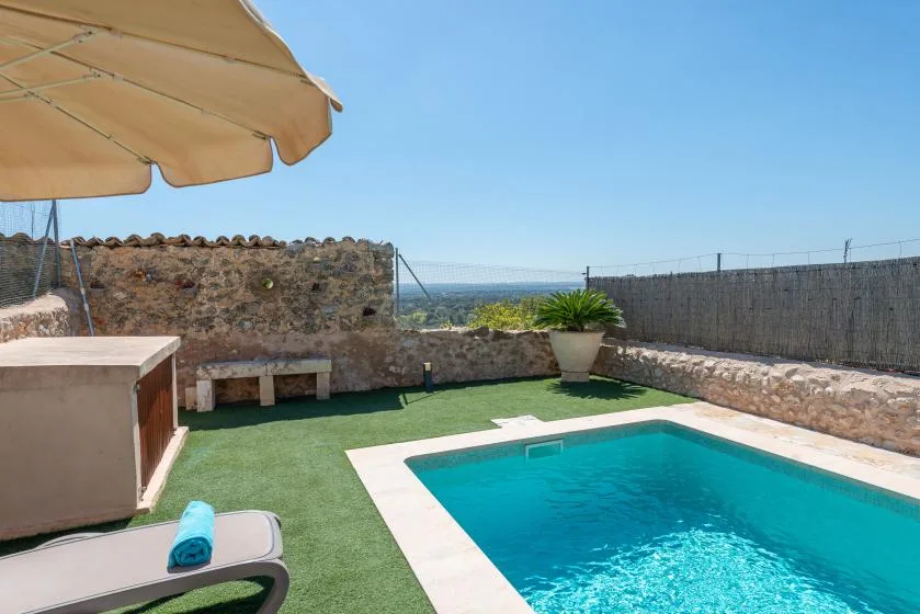 An outdoor swimming pool sits beside a stone wall on a sunny patio.