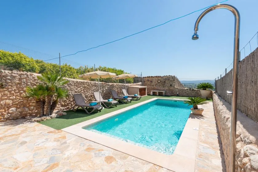 An outdoor swimming pool is surrounded by stone walls and lounge seating.