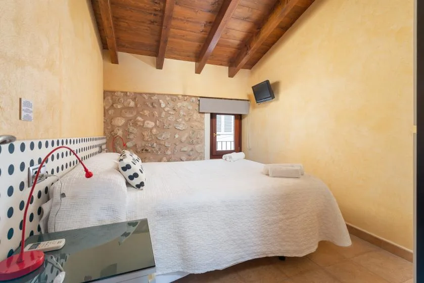 A bedroom with a bed, stone accent wall, and exposed wooden ceiling beams.
