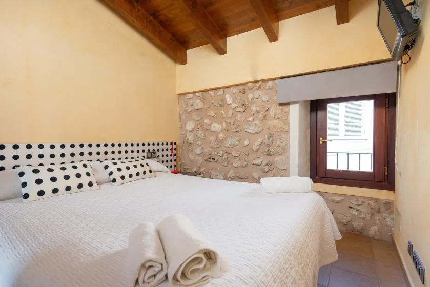 A bedroom with a large bed, patterned pillows, and a window beside a stone wall.