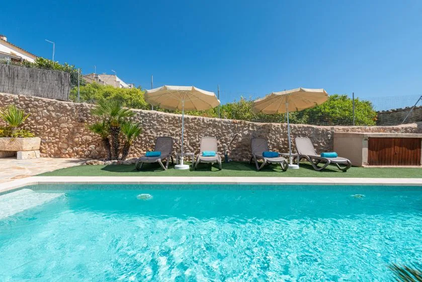 An outdoor swimming pool with lounge seating and umbrellas beside a stone wall.