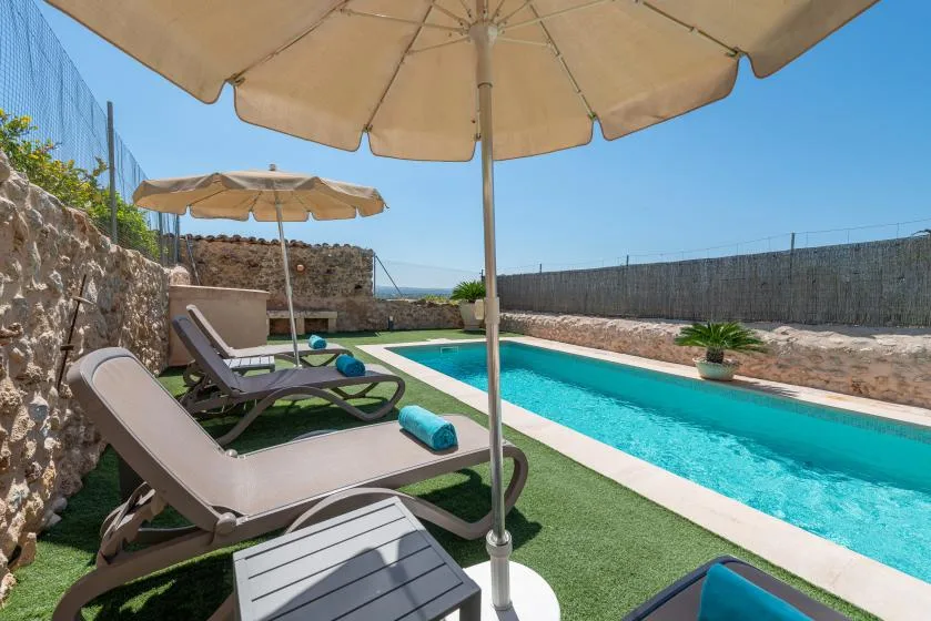 A poolside patio has lounge seating beneath large umbrellas.