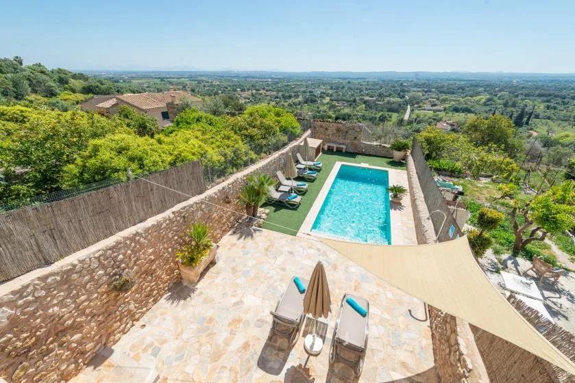 A swimming pool and sun loungers sit on a terrace overlooking the countryside.